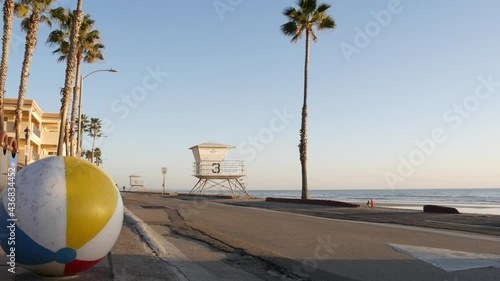 Pacific ocean beach, Oceanside California USA. Ball, lifeguard tower, life guard watchtower hut and tropical palm tree, sky, beachfront street, waterfront road. Los Angeles vibes, aesthetic atmosphere