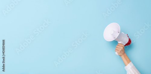 Business Hand holds a megaphone from a hole in the wall on blue background.  hiring, advertising, advertise and Banner concept.