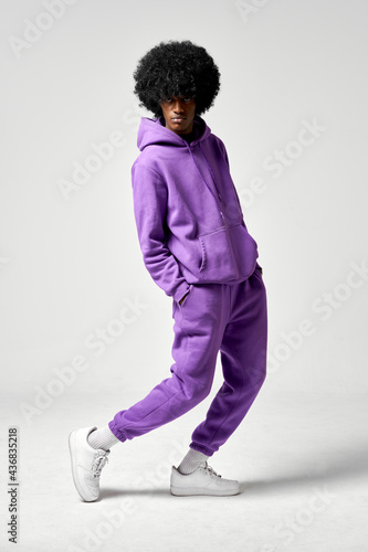 Tableau sur toile Young black man in set of purple tracksuit presenting white sneakers isolated on
