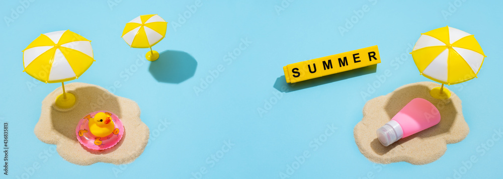 Summer skin care concept. Sunscreen on the sand and an umbrella from the sun on a blue background.  Text from letters on yellow cubes