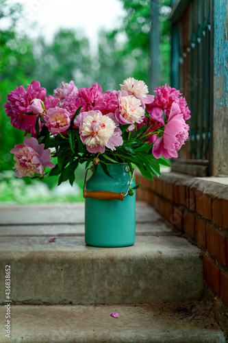 Fototapeta Naklejka Na Ścianę i Meble -  Bouquet of pink peonies in milk can standing on stairs of a country house