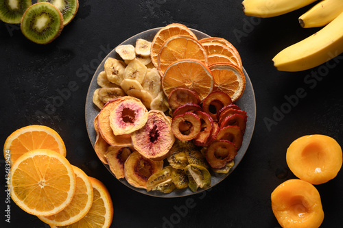 Dried different fruits sliced plums, kiwi, peach chipson black background, home drying. Snack vegan sugar free food. View from above. photo