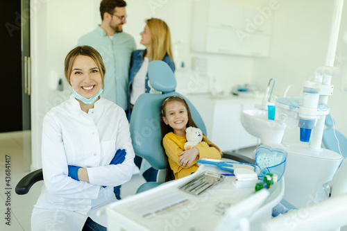 Portraits of cute little girl sitting in dental chair and smiling young kind female dentist.