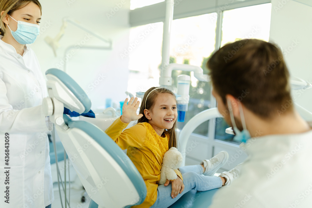 Man doctor is giving hi five to little girl after a successful dental examination. Focus on girl. Man doctor is giving hi five to little girl after a successful dental examination. Focus on girl.