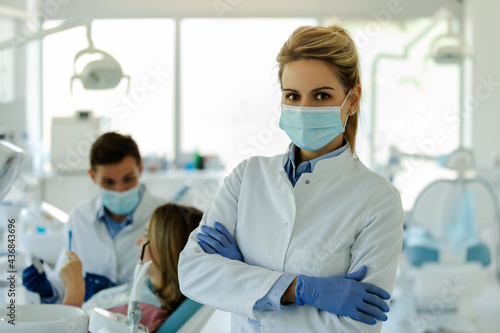 Female dentist posing in modern dental office with crossed arms  protective mask and gloves.