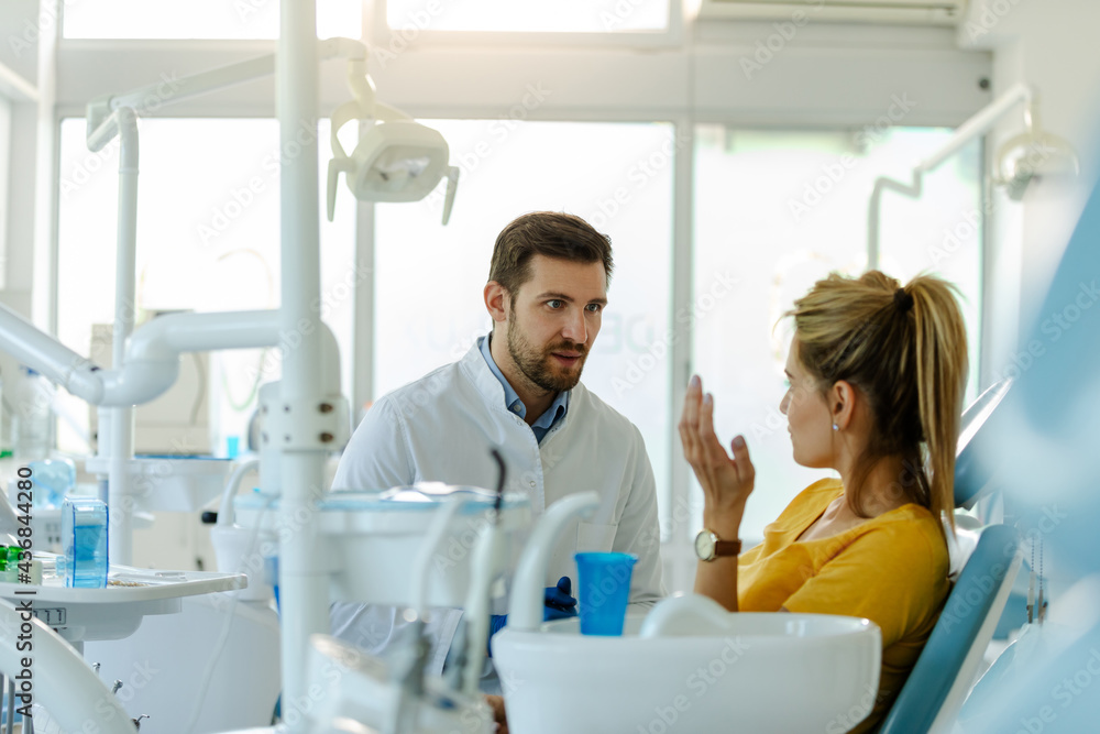 Male dentist in dental office talking with female patient and preparing her for treatment. Male dentist in dental office talking with female patient and preparing her for treatment.