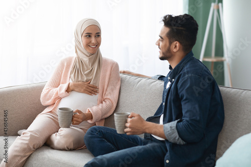 Happy Expectant Middle Eastern Couple Resting Together On Couch At Home