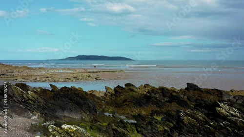 Aerial low view of drone flying over rocky beach landscape and revealing the Irish sea and Lambay Island.  Donabate beach in summer, Dublin, Ireland