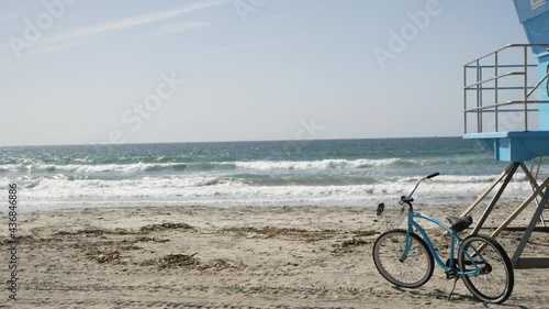 Blue bicycle, cruiser bike by ocean beach, pacific coast, Oceanside California USA. Summertime vacations, sea shore. Vintage cycle on sand near lifeguard tower or watchtower hut. Sky and water waves.