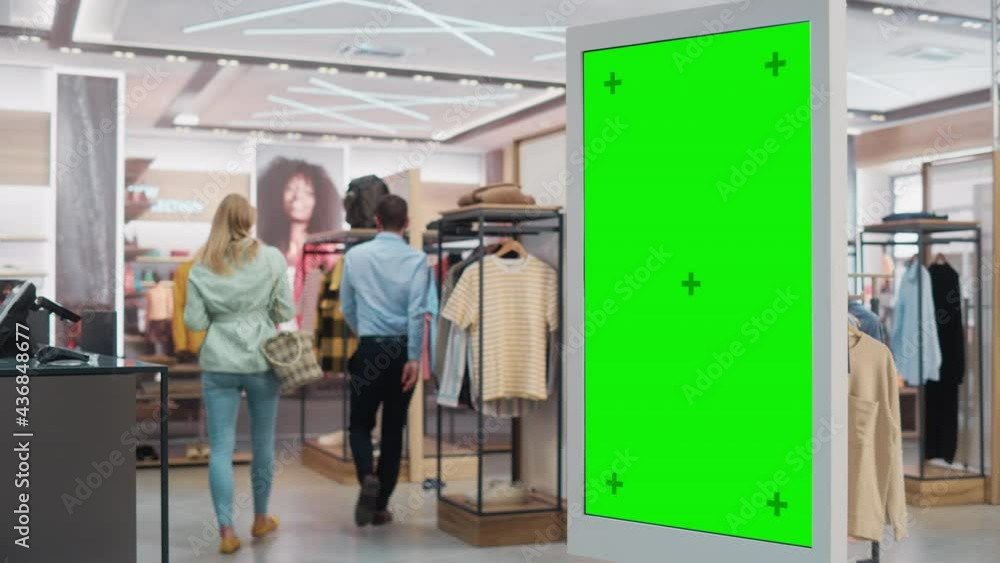 Customer Using Floor-Standing LCD Touch Display with Green Screen Chroma Key Mock Up while Shopping in Clothing Store. She is Checking for Information, Looking at a Floor Plan, Choosing Items Online. Customer Using Floor-Standing LCD Touch Display with Green Screen Chroma Key Mock Up while Shopping in Clothing Store. She is Checking for Information, Looking at a Floor Plan, Choosing Items Online.