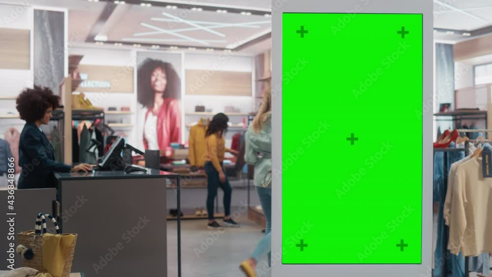 Customer Using Floor-Standing LCD Touch Display with Green Screen Chroma Key Mock Up while Shopping in Clothing Store. She is Checking for Information, Looking at a Floor Plan, Choosing Items Online. Customer Using Floor-Standing LCD Touch Display with Green Screen Chroma Key Mock Up while Shopping in Clothing Store. She is Checking for Information, Looking at a Floor Plan, Choosing Items Online.
