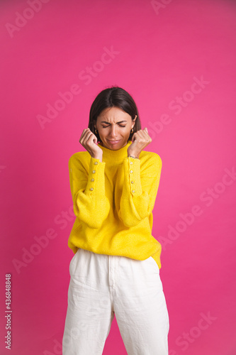 Beautiful woman in bright yellow sweater isolated on pink background stressful crying depression