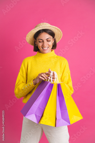 Beautiful woman in bright yellow sweater and straw hat on pink background hold shopping bags happy excited joyful isolated space for text