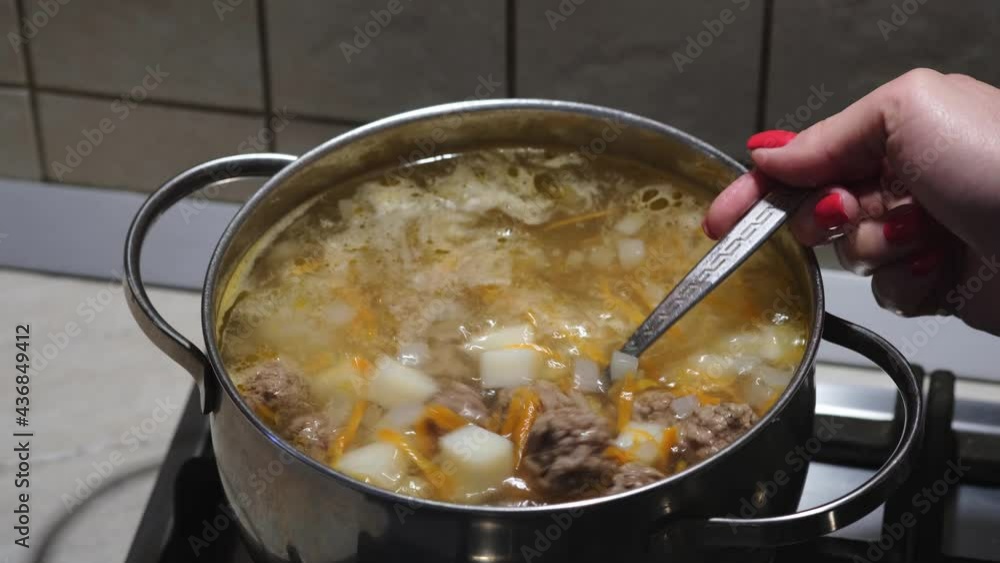 Cooking of meatball soup with vegetables. Women's hands stirring homemade bouillon. Close-up. Selective focus Cooking of meatball soup with vegetables. Women's hands stirring homemade bouillon. Close-up. Selective focus