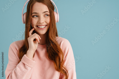 Young ginger woman smiling while listening music with headphones