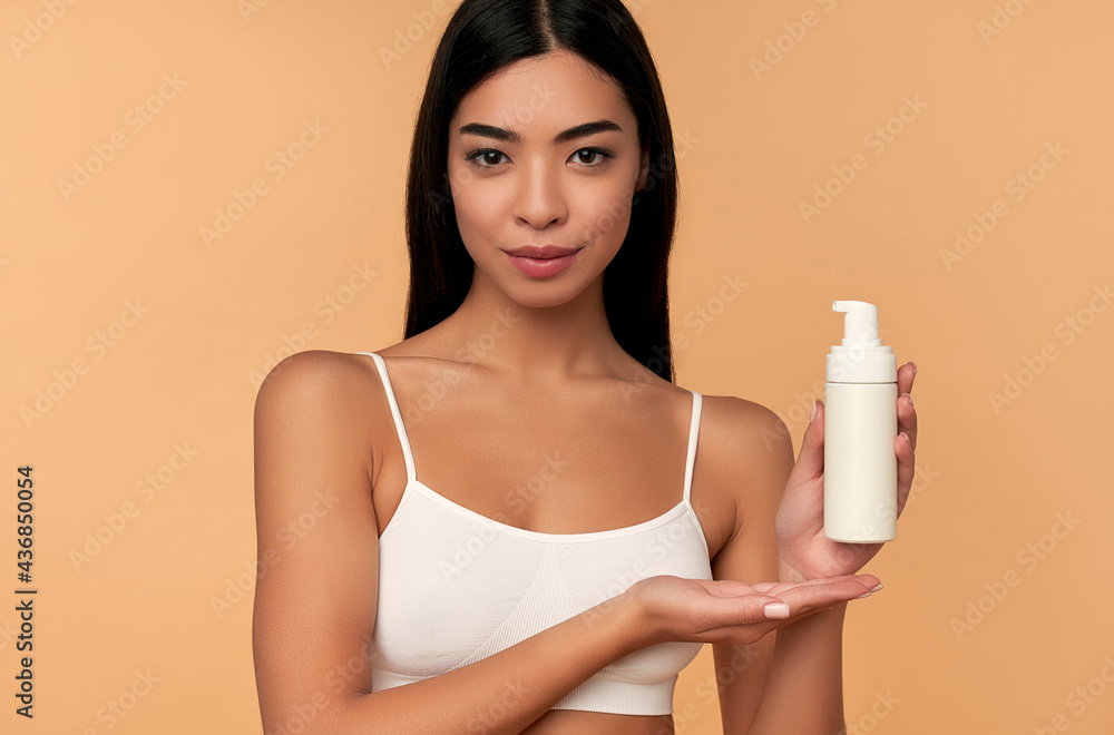 Young asian woman in white lingerie with shining skin with bottle of facial foam.isolated on a beige background. Facial skin care concept. Beauty. Young asian woman in white lingerie with shining skin with bottle of facial foam.isolated on a beige background. Facial skin care concept. Beauty.