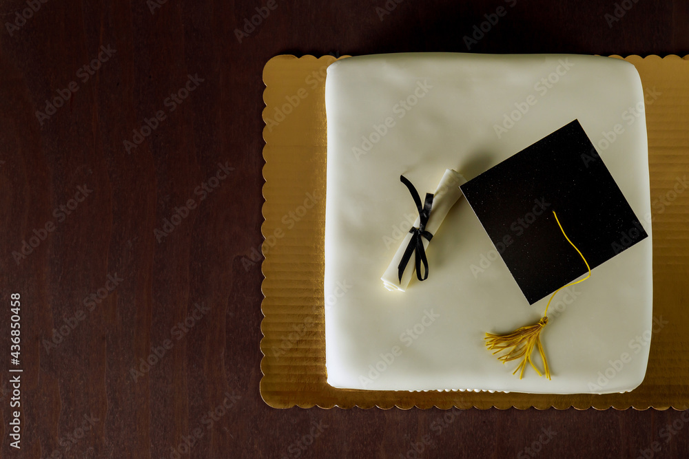 Graduation white cake with cap on the top and diploma decor.