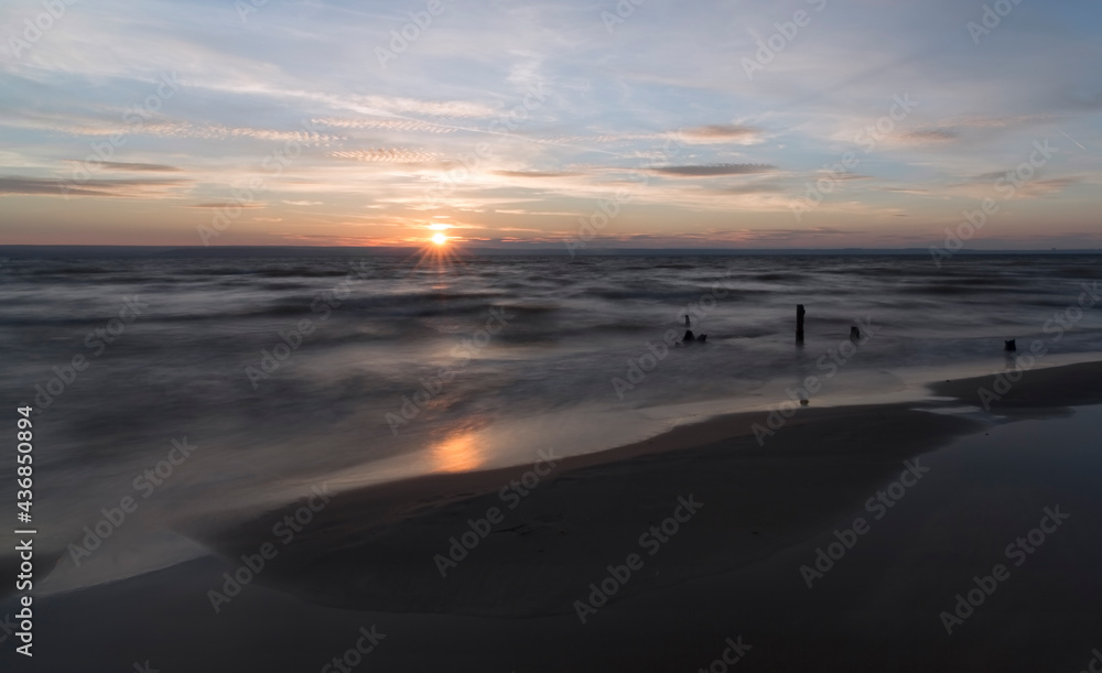 Old tree stump in the water against the backdrop of a beautiful sunset and blue sky.
