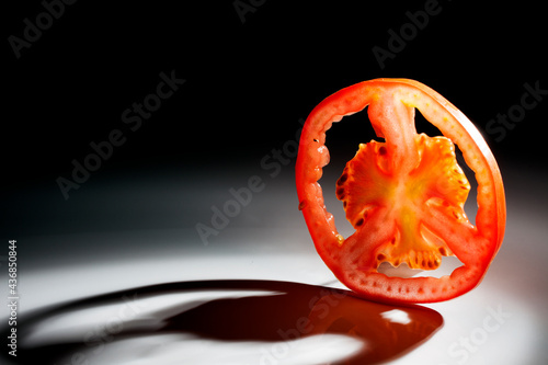 A slice of tomato fruit slice isolated on black background with a beautiful back light