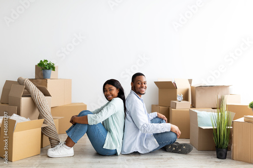 Happy spouses moving to new apartment or house. Loving african american couple sitting on floor among paper boxes