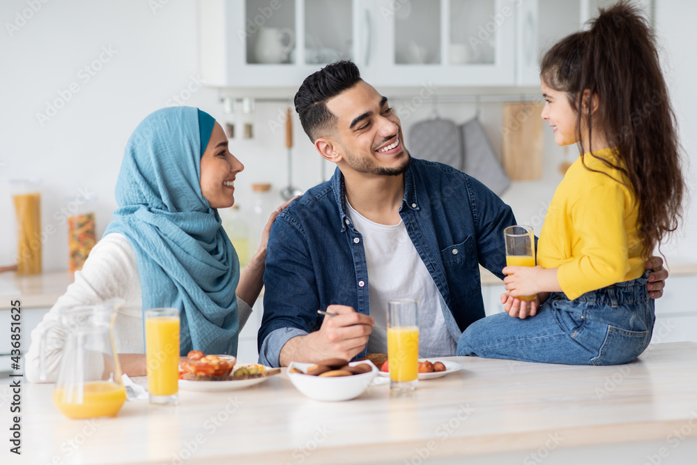 Portrait Of Happy Muslim Family Of Three Eating Lunch In Kitchen Together