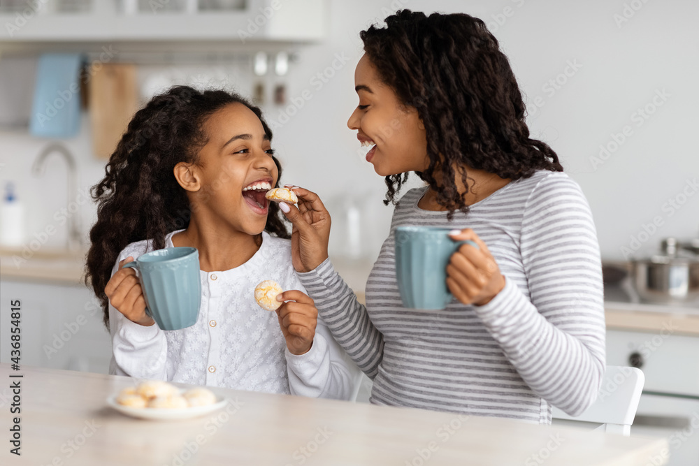 Happy black mom feeding her kid with cookies