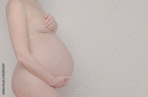 Wallpaper Mural body of a pregnant woman in her third trimester, only the body is shown, with her hand she covers her breast and with the other hand she holds her belly, light background, studio photography.  Torontodigital.ca