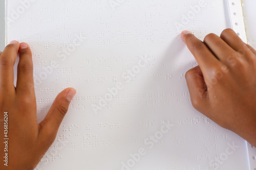 Hands of blind african american schoolboy reading braille book with fingers