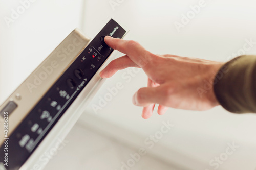 Obraz na plátně Man pushing start button on the control panel of the dishwasher.