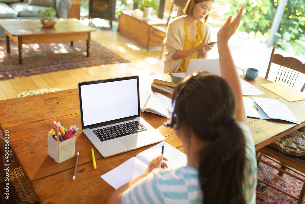 Asian girl using laptop with blank screen, raising hand, learning online her mum in background Asian girl using laptop with blank screen, raising hand, learning online her mum in background