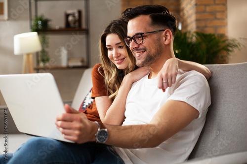 Happy young couple with laptop at home. Boyfriend and girlfriend watching movie on laptop