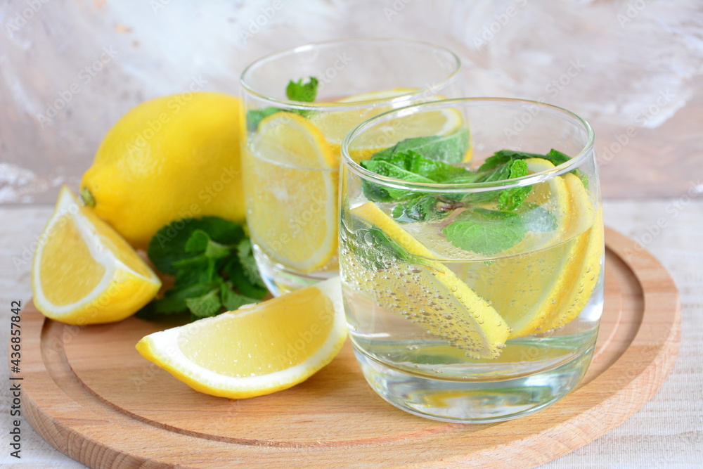 Fototapeta premium glasses with mineral water, lemon slices, mint leaves on the cutting board on the beige background