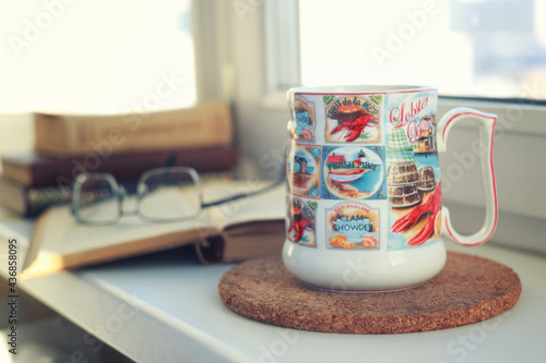 Big cup of coffee or mug of beer, books and glasses on windowsill. Morning tea or coffee. Cosiness and good morning concept