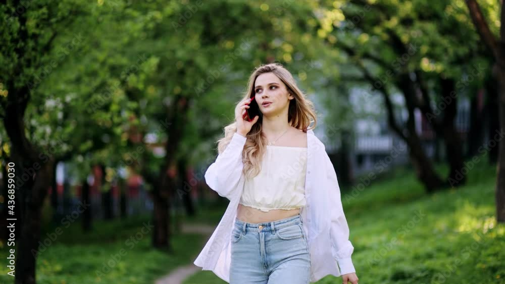 Portrait of excited young beautiful blonde woman using mobile phone in park. Positive woman walking with smartphone on park road Portrait of excited young beautiful blonde woman using mobile phone in park. Positive woman walking with smartphone on park road