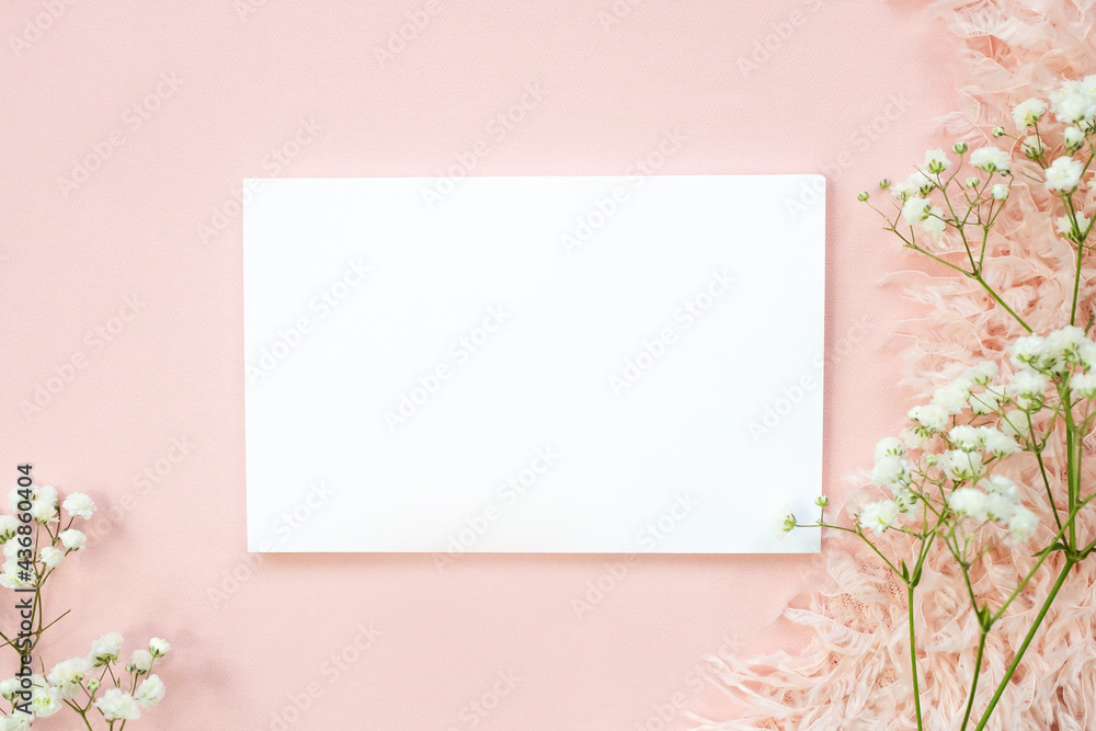 Fototapeta premium Blank white sheet on beige background and natural pink flower. Top view, space for text.