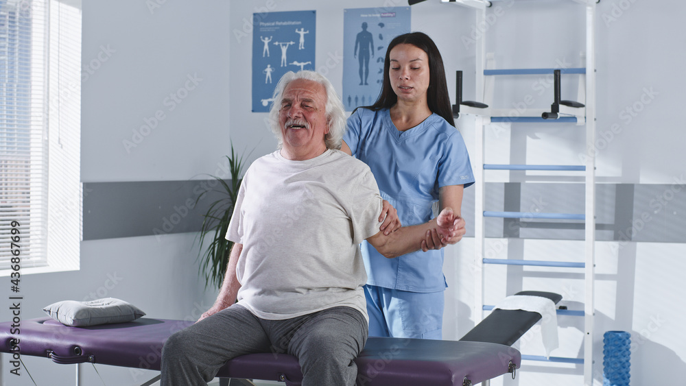 Rehabilitation therapist stretching arm of elderly man Rehabilitation therapist stretching arm of elderly man