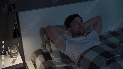 Lonely man cannot sleep in bed at night with eyes wide open, staring at ceiling. Male lying in bed, stressed, worried and cant sleep. Insomnia. Sleepless guy addicted to smartphone instead of sleep