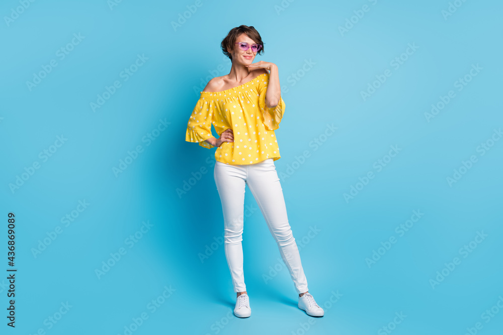 Full length photo of stunning charming young lady wear white pants yellow dotted blouse isolated on blue color background Full length photo of stunning charming young lady wear white pants yellow dotted blouse isolated on blue color background