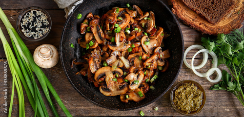 Roasted mushrooms with onion in frying pan on a wooden background. Top view. Food banner