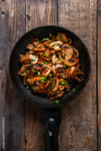 Roasted mushrooms with onion in frying pan on a wooden background. Top view