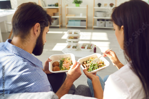 Young couple man and woman office workers sitting and enjoying healthy boxed food order delivered to worklace, rear view. Healthy food delivery service and daily ration concept photo