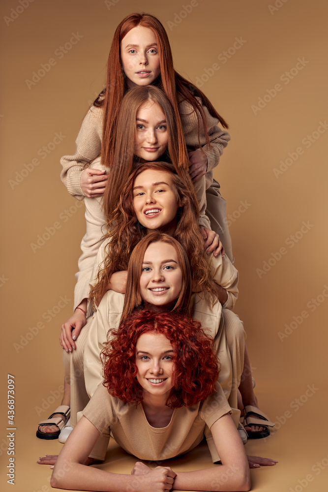 Attractive red-haired models isolated on beige studio background, on each other. Adorable ladies with natural beauty and red hair, nude make-up, look at camera smiling. friendship, unity concept