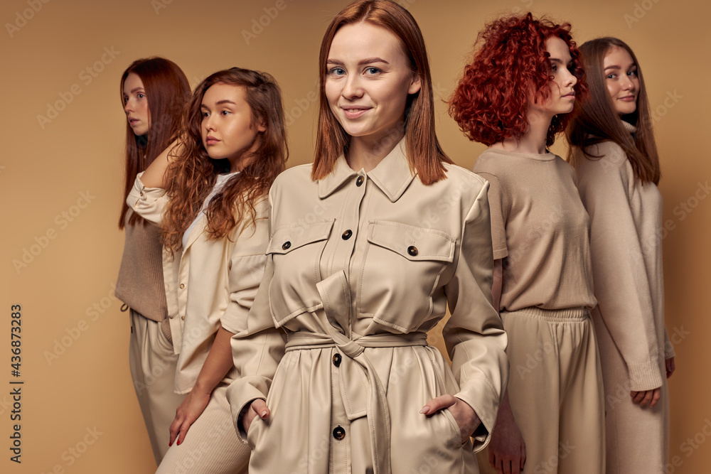 Stylish red-haired models in beige casual outfit stand isolated on beige background, young women posing at camera. Natural beauty, fashion, style concept Stylish red-haired models in beige casual outfit stand isolated on beige background, young women posing at camera. Natural beauty, fashion, style concept