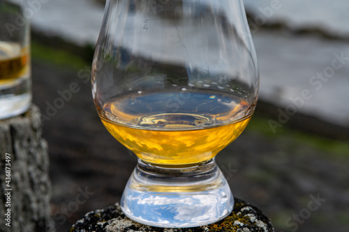 Tasting of dram single malt scotch whisky on seashore in Scotland, old wooden pole with whisky glass