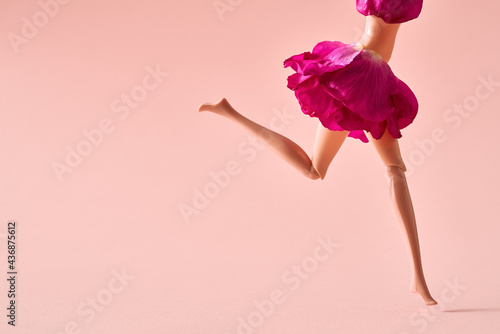 Plastic woman figure dressed in rose petals runnig in joy on pastel pink background in the summer photo