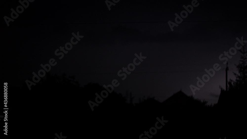 4K video. Flashing lightnings, rain and hail at night. Dramatic electric lightning bolt in the village. Silhouette of houses and trees. Poles with wires, power lines. Extreme weather and thunderstorm