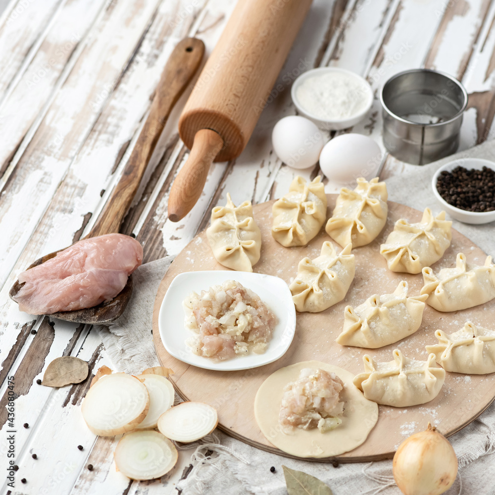 Fototapeta premium Convenience Food Cooking process. Dumplings stuffed with minced chicken fillet and onion. Ingredients and kitchen utensils on rustic background. Square format. Dough stuffed with meat. Top view.