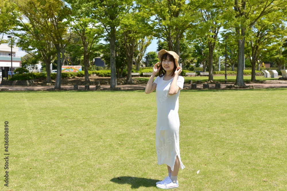 新緑の公園でポーズをとる麦わら帽子を被った若い笑顔の女性 Photos Adobe Stock