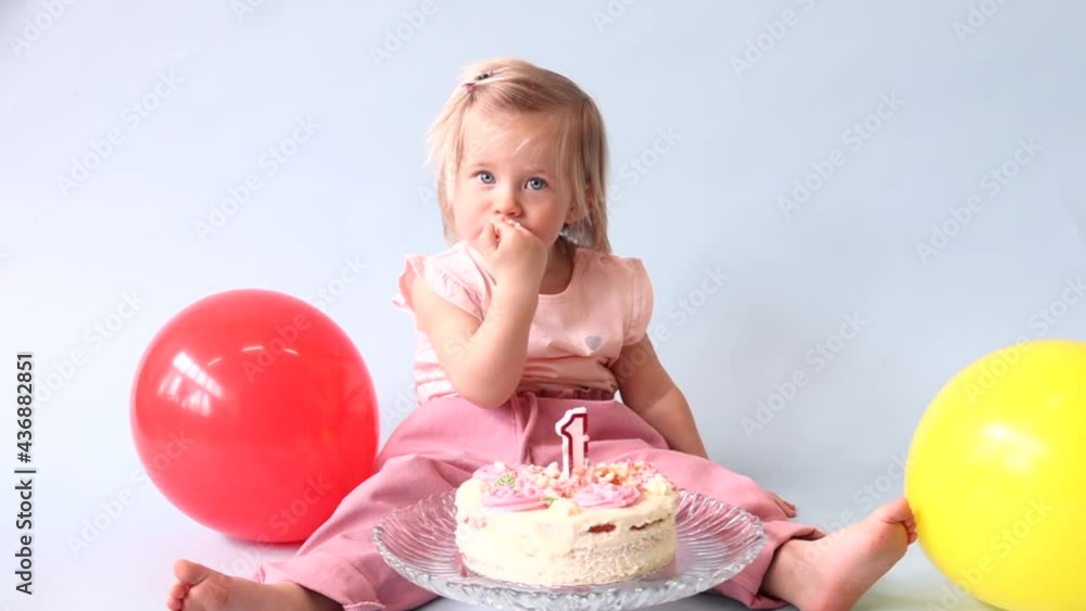 little beautiful blue-eyed girl celebrates her first birthday in the style smash a cake and she tastes her first birthday cake