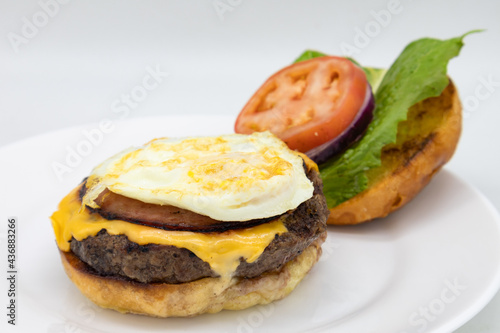 Open Faced American Style Cheeseburger with a Fried Egg and Lettuce and Tomatoes on a White Plate